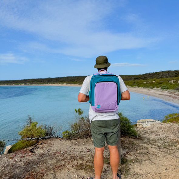 man wearing the lilac on teal adventure backpack on a coastal walk