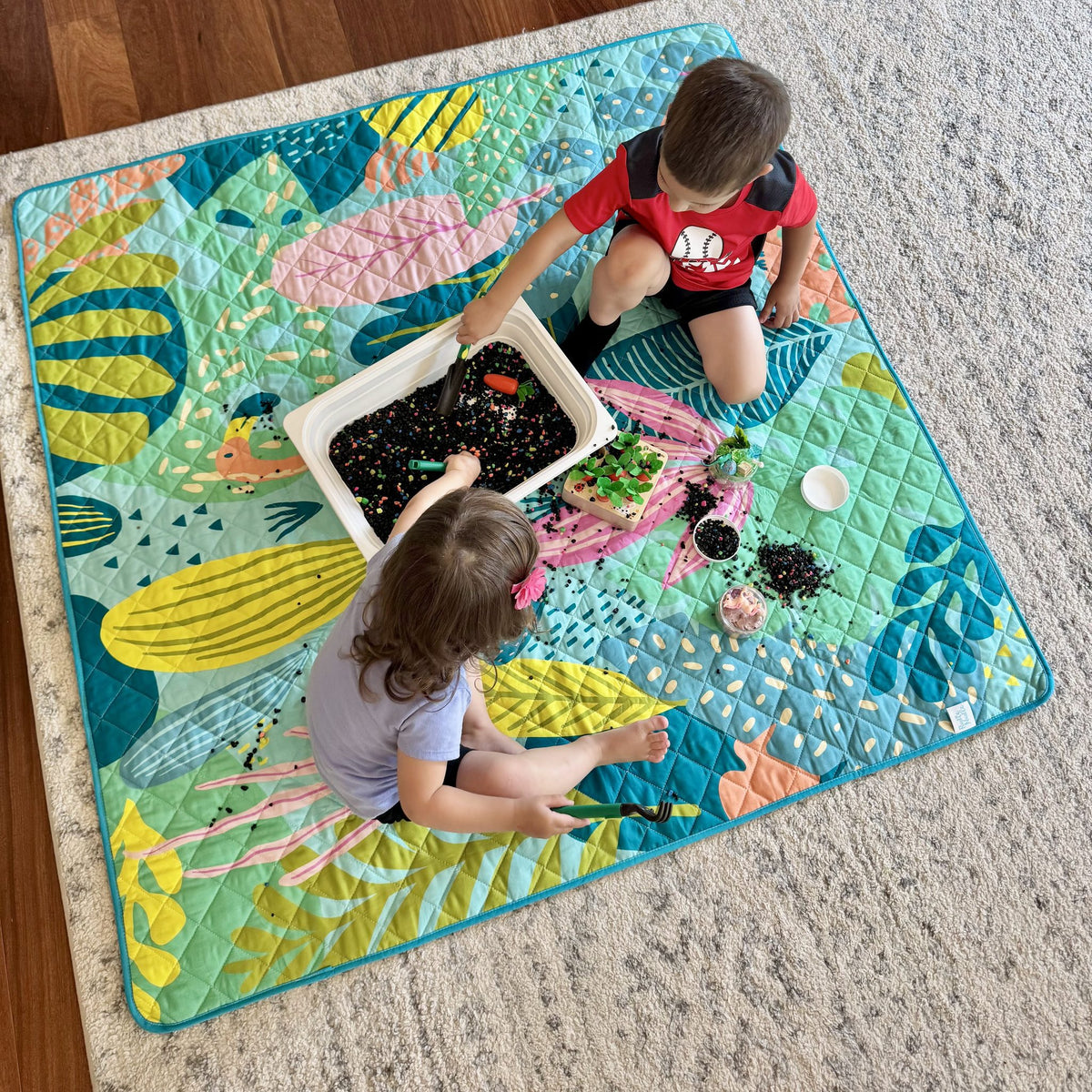 two children doing messy sensory play on the flamingo-a-go-go large waterproof playmat in the living room