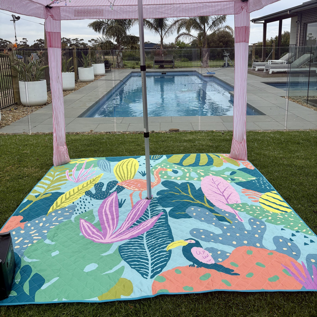 flamingo-a-go-go picnic blanket with umbrella hole set up under a cabana beside a pool