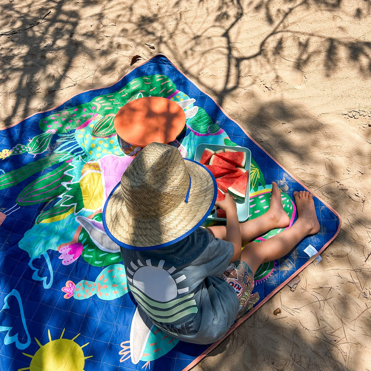 child eating watermelon on the hola mamacita large waterproof playmat on the sand