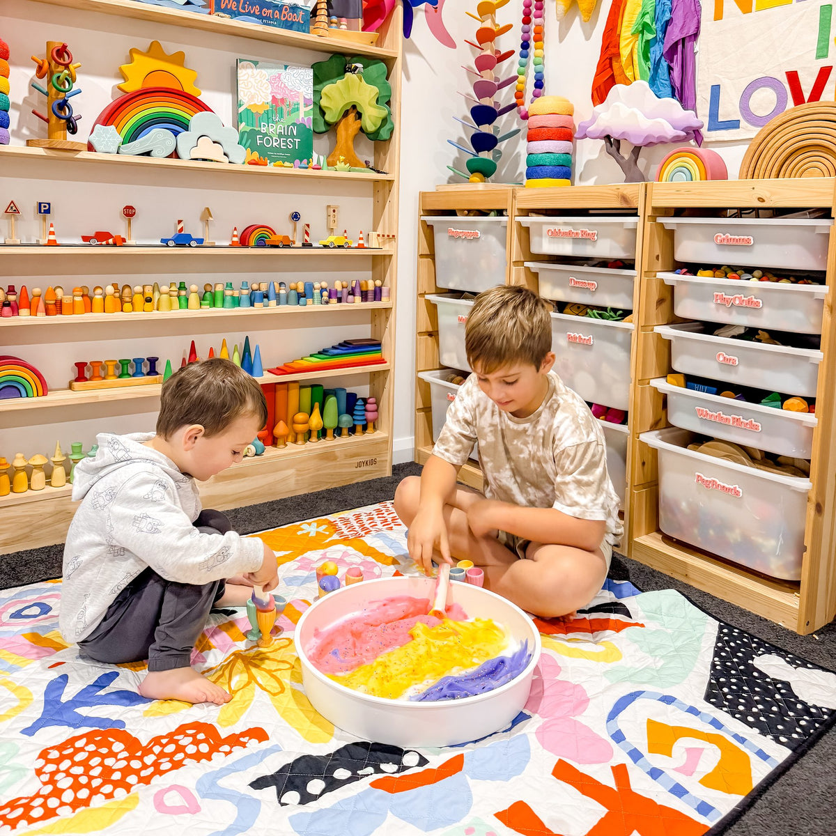 two children playing with a sensory tray on the pop pip pow large waterproof playmat in a playroom