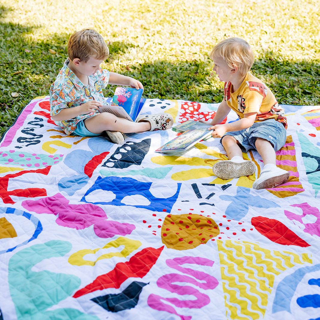 two toddlers reading on the pop pip pow waterproof picnic blanket in the park