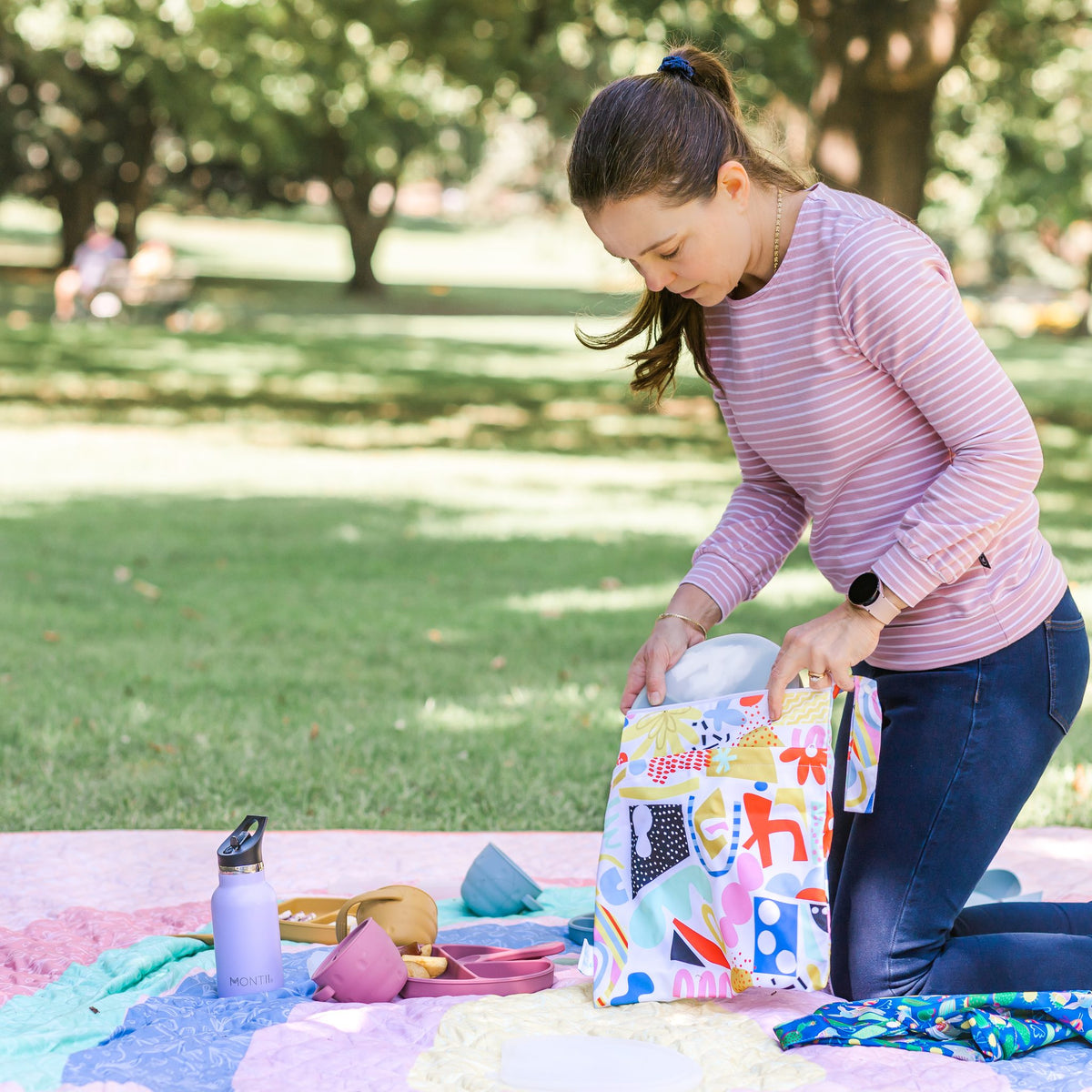 mother packing up a picnic into a pop pip pow wet bag in the park