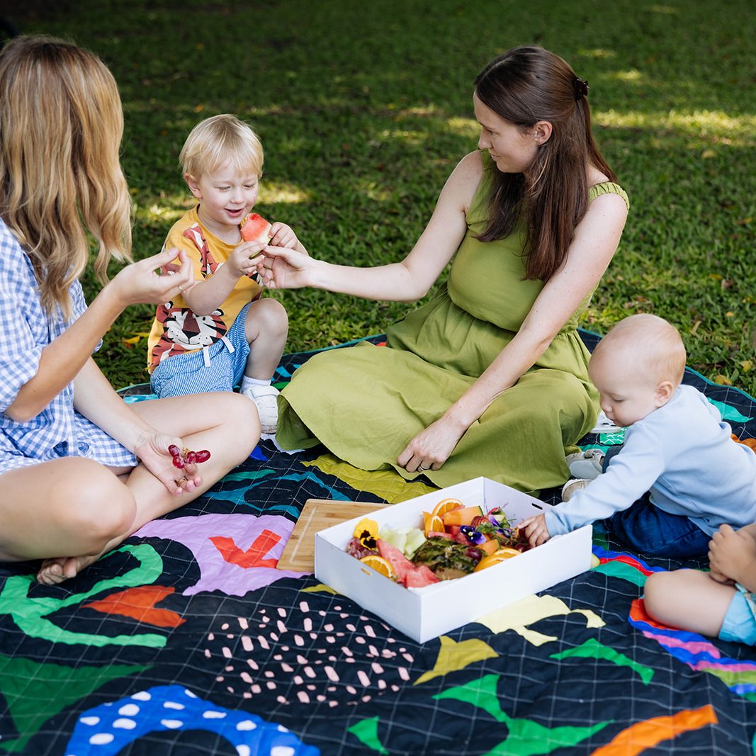 two mothers and children sharing a snack box on the rock candy waterproof picnic blanket