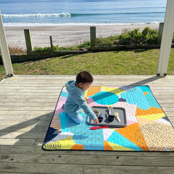 child playing on the happy now large waterproof playmat on a deck overlooking the beach