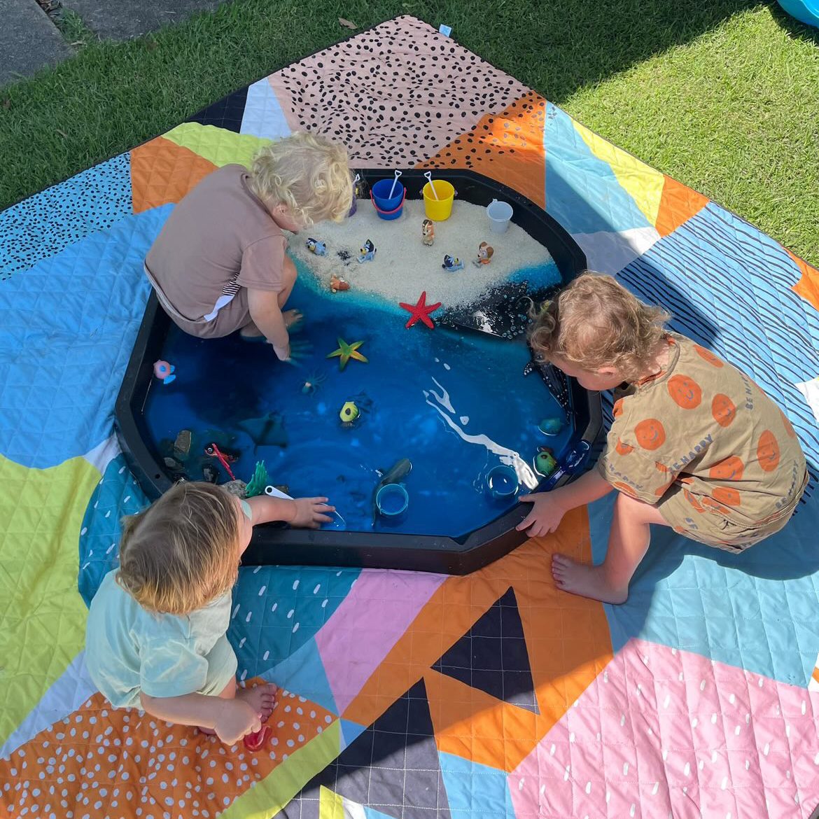 three toddlers playing with an ocean sensory tray on the happy now waterproof picnic blanket