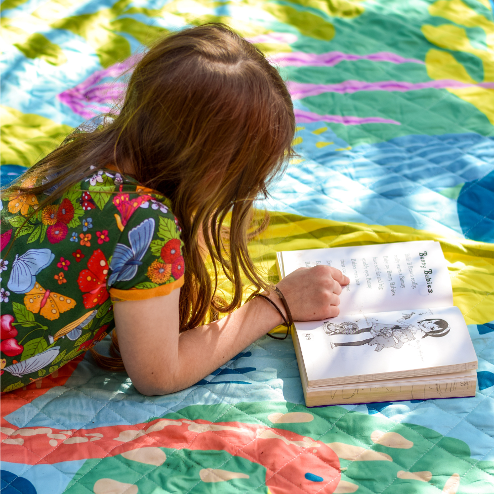 girl reading in garden with book on a colourful blanket