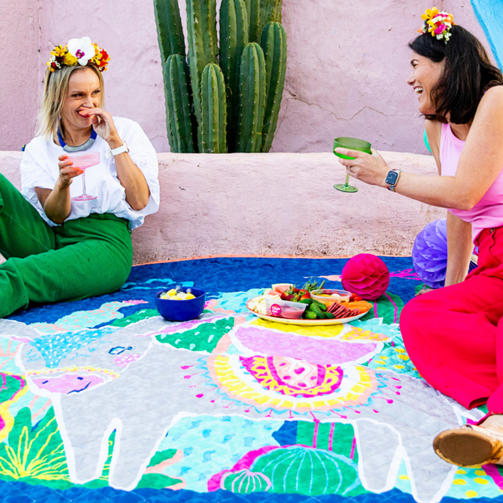 women enjoy food as they sit on a picnic blanket and celebrate