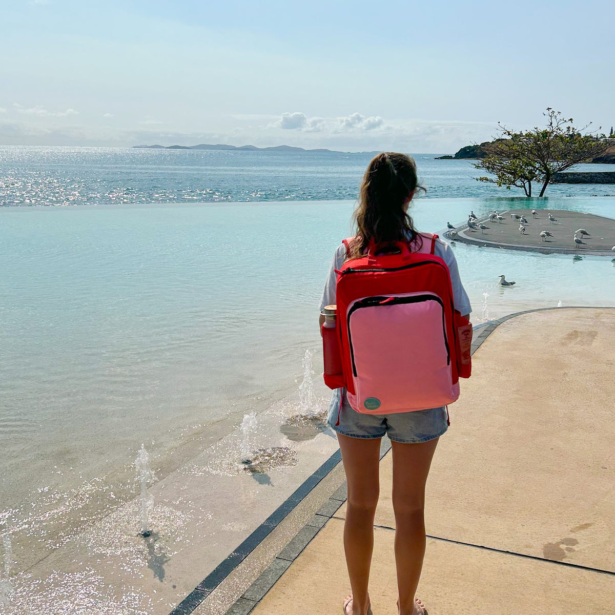woman wearing the blush on red adventure backpack by the water