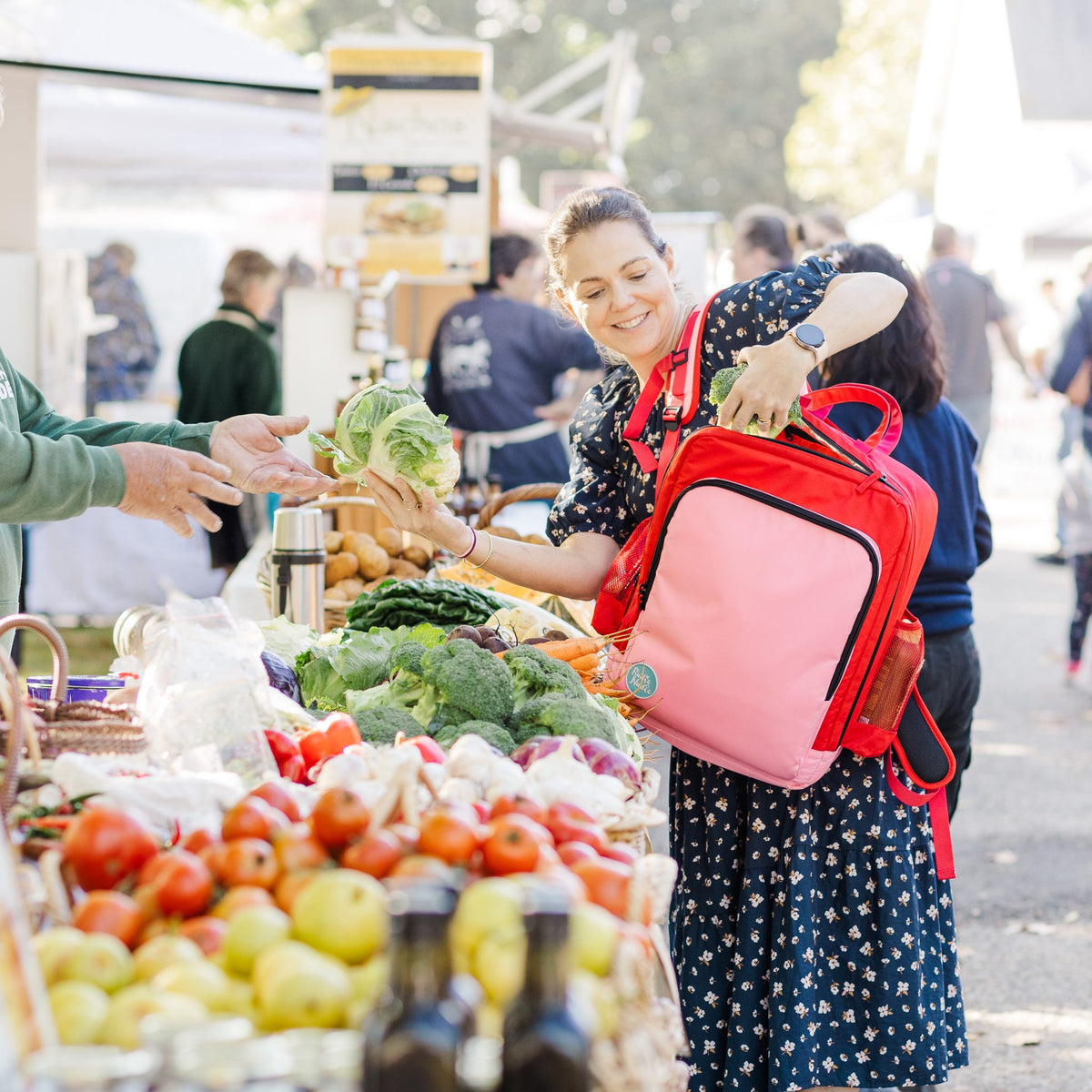 mother shopping at a farmers market wearing the blush on red adventure backpack