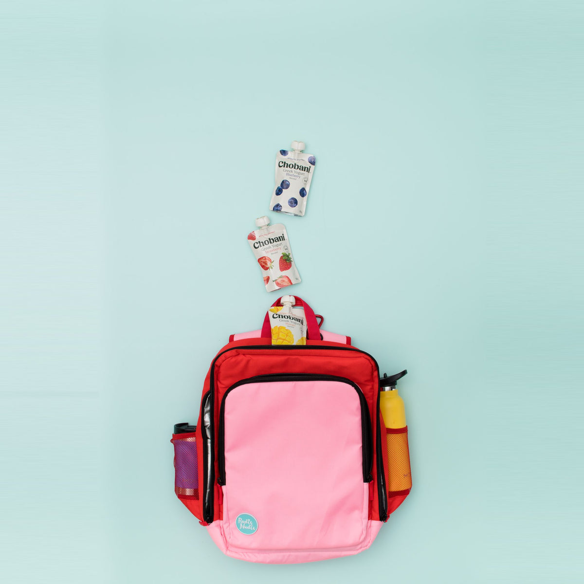 flat lay of the blush on red adventure backpack with snack pouches and drink bottles in the side pockets