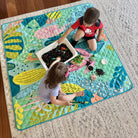 two children doing messy sensory play on the flamingo-a-go-go large waterproof playmat in the living room