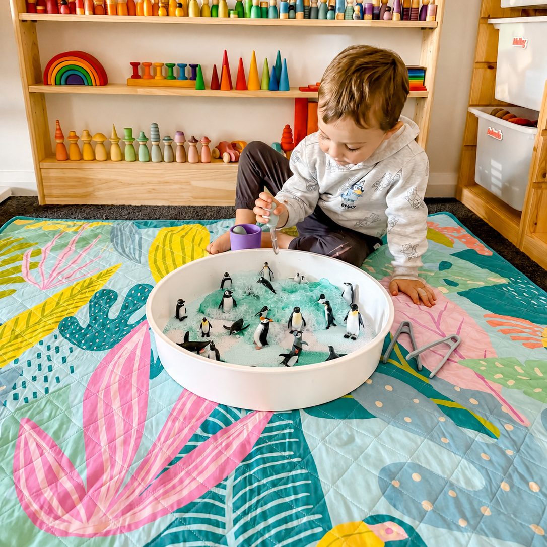 toddler playing with a sensory tray on the flamingo-a-go-go large waterproof playmat