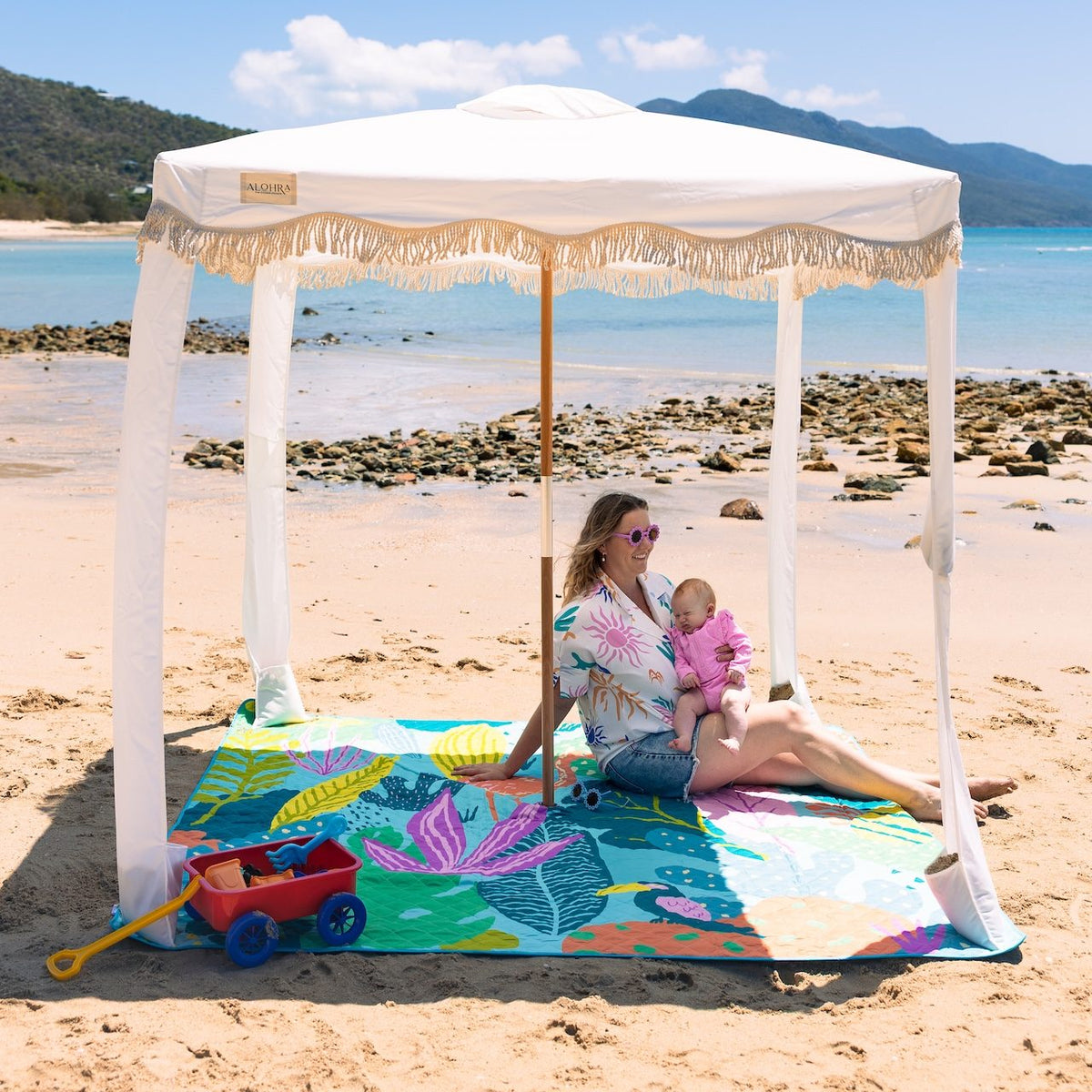 mother and baby under a beach cabana on the flamingo-a-go-go picnic blanket with umbrella hole