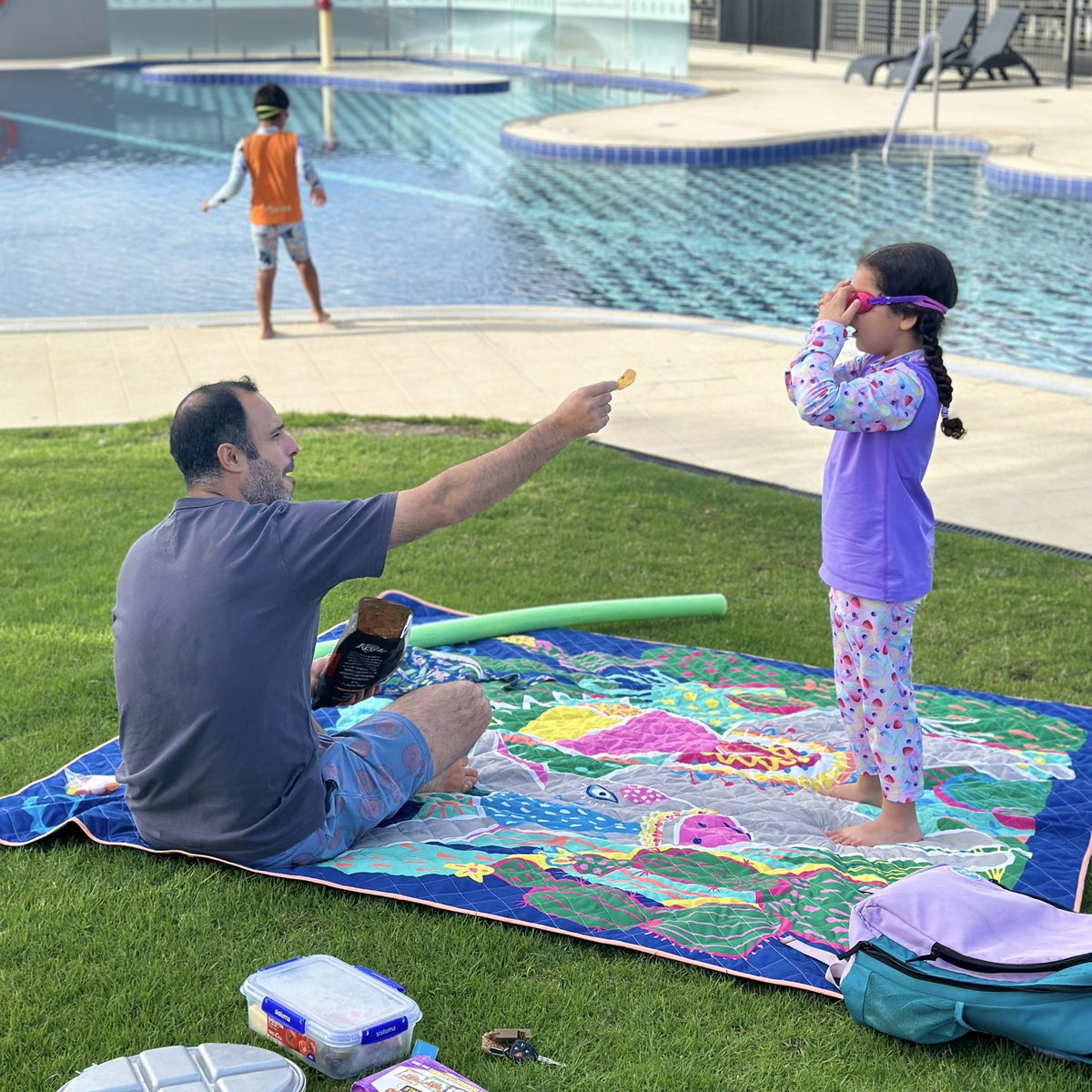 dad and daughter on the hola mamacita waterproof picnic blanket beside a pool