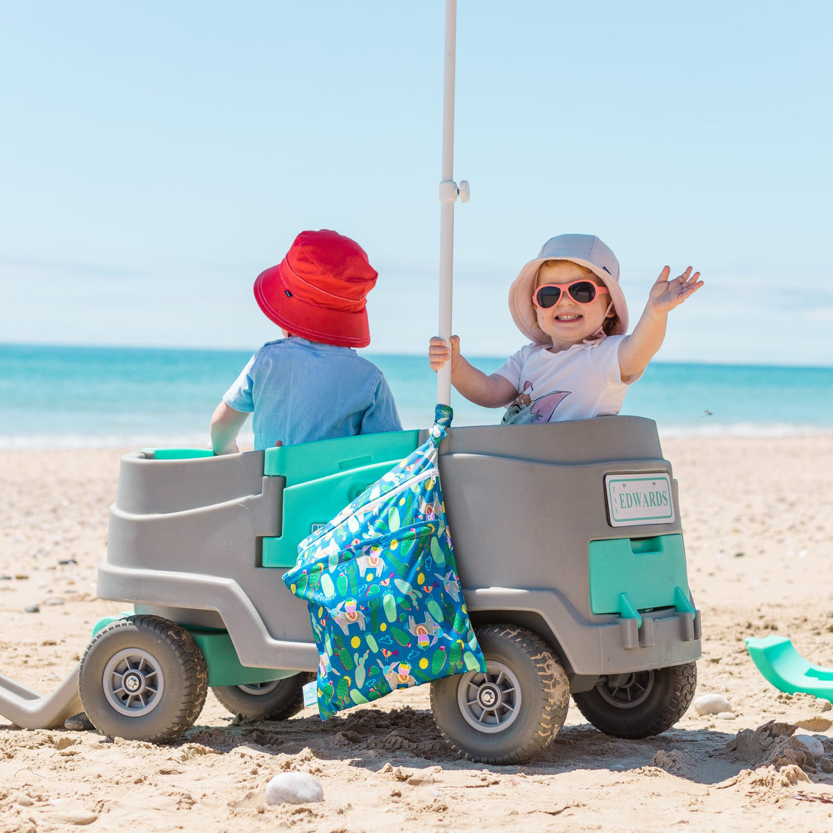 hola mamacita wet bag hanging on a beach wagon with two toddlers