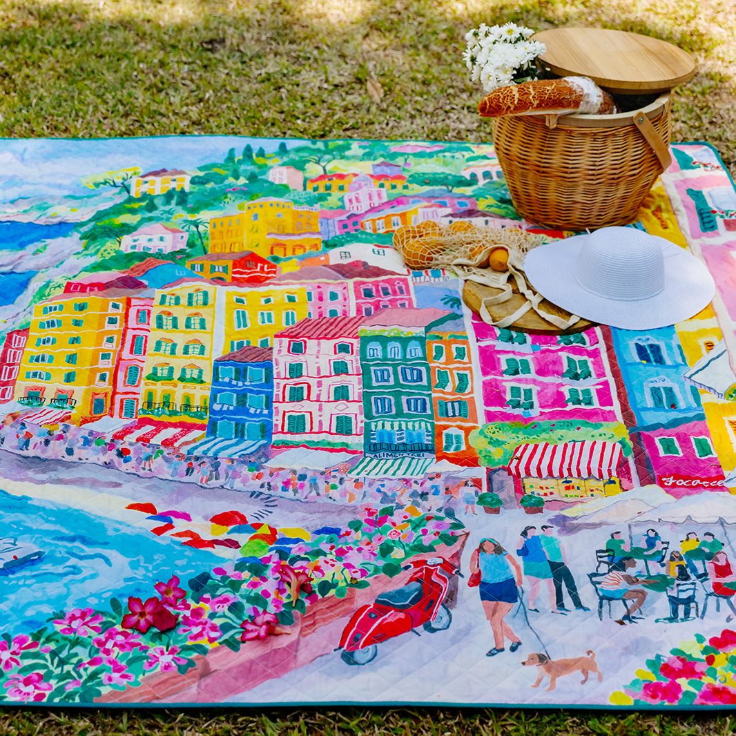 la dolce vita waterproof picnic blanket laid out on the grass with a picnic basket and sun hat