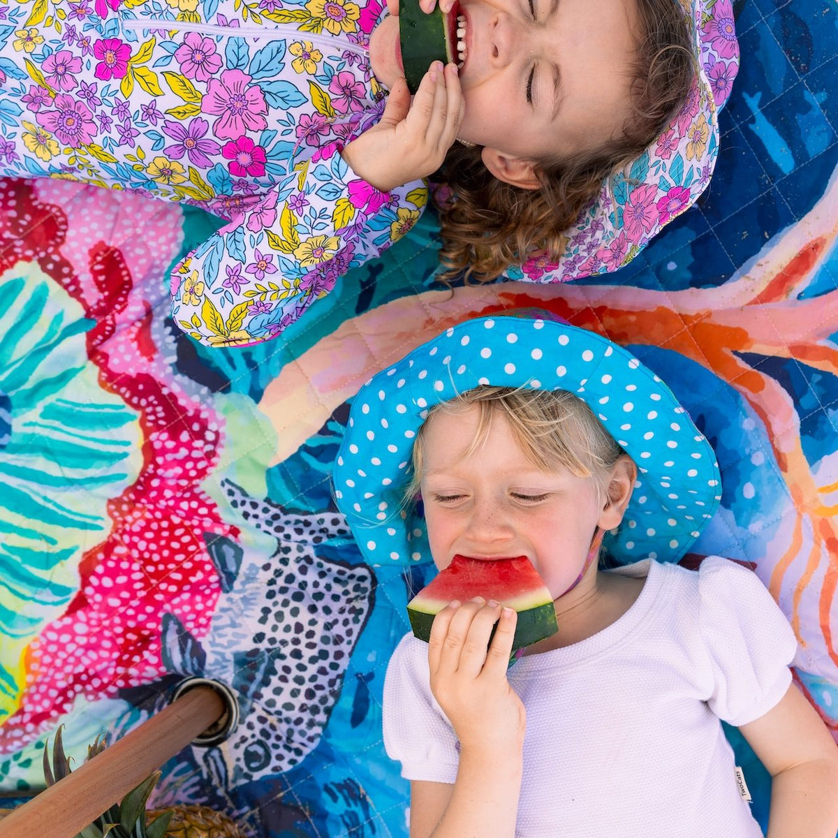 two children eating watermelon lying on the octopus's garden picnic blanket with umbrella hole