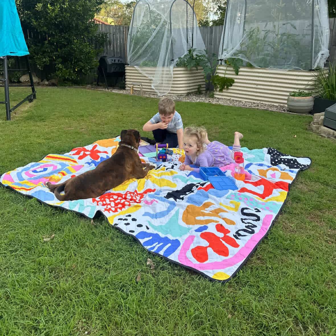 children and a dog on the pop pip pow waterproof picnic blanket in the backyard