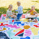 three toddlers playing on the pop pip pow waterproof picnic blanket in the park
