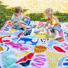two toddlers reading on the pop pip pow waterproof picnic blanket in the park