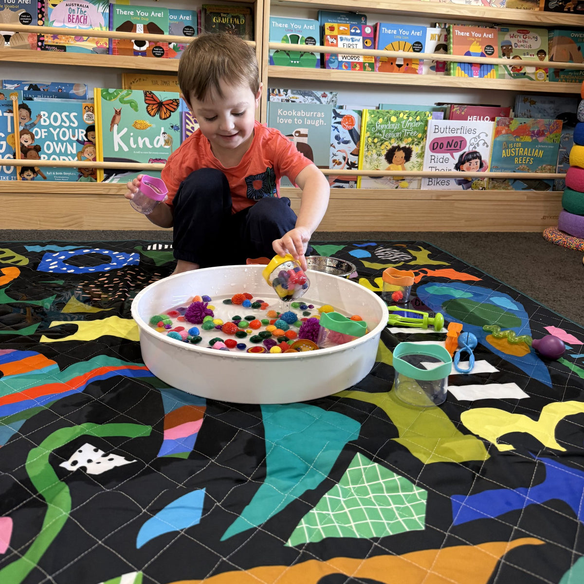 child doing pom pom sensory play on the rock candy large waterproof playmat