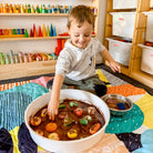 smiling toddler doing messy mud play on the happy now large waterproof playmat