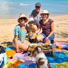 family with a toddler and dog on the happy now waterproof picnic blanket at the beach